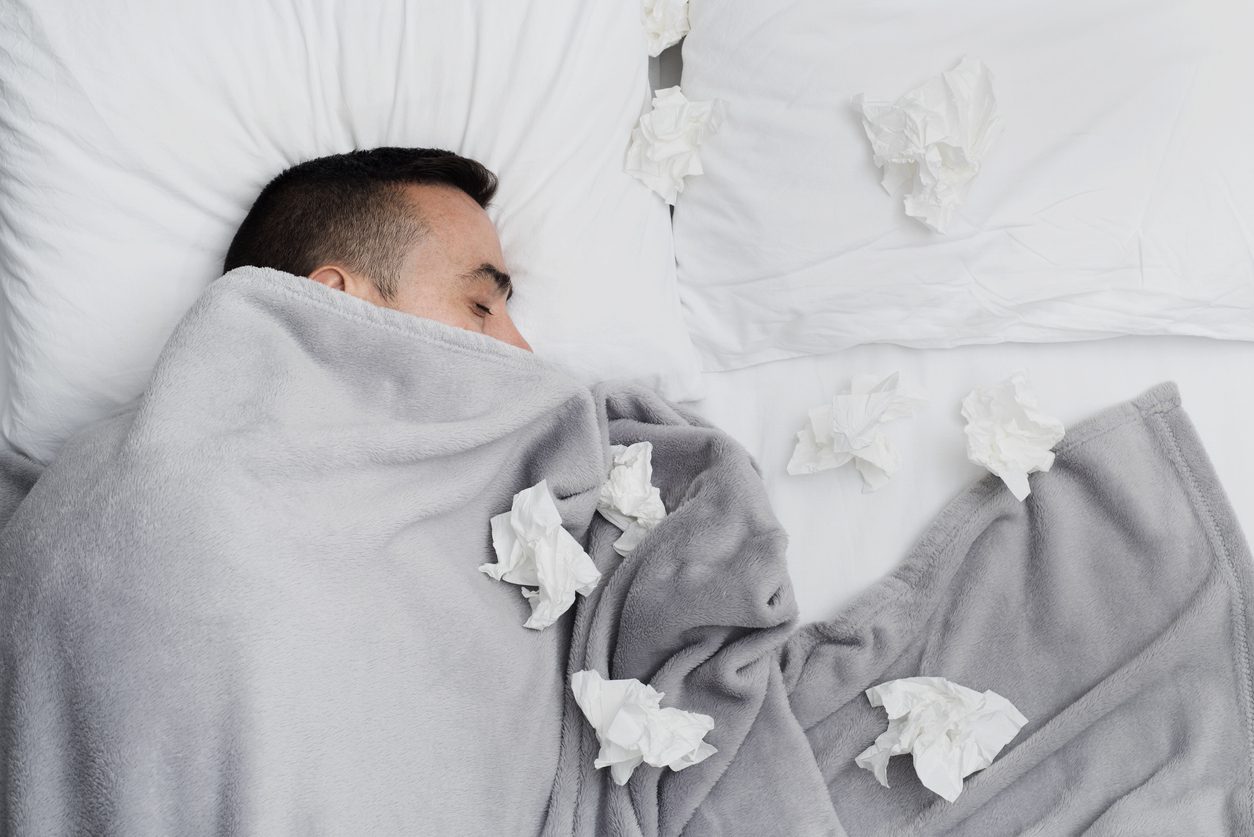 ill man in bed surrounded by used tissues